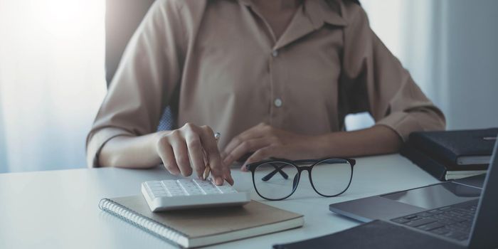 Business woman using calculator for do math finance on wooden desk in office and business working background, tax, accounting, statistics and analytic research concept.