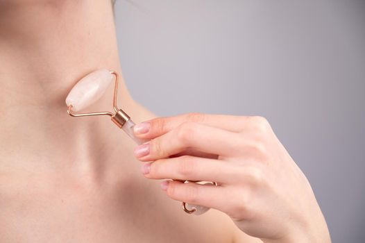 Close-up portrait of a woman using a quartz roller massager for an alternative fight against wrinkles on her neck. Smoothing of the rings of venus