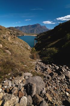 Mountain valley with a lake. The lake is surrounded by rocky mountains, the sky is almost cloudless. Vertical panorama.