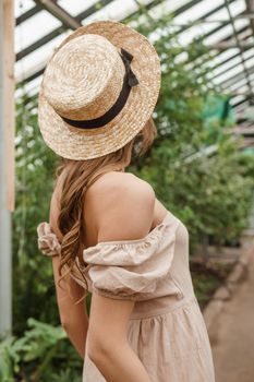 A beautiful young woman takes care of plants in a greenhouse. The concept of gardening and an eco-friendly lifestyle.