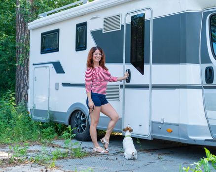 Beautiful caucasian woman is training a dog next to the motorhome. Travel with your pet in a mobile RV. Female trailer driver