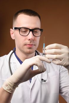 Caucasian male doctor holding a syringe in his hands in uniform, studio shot.
