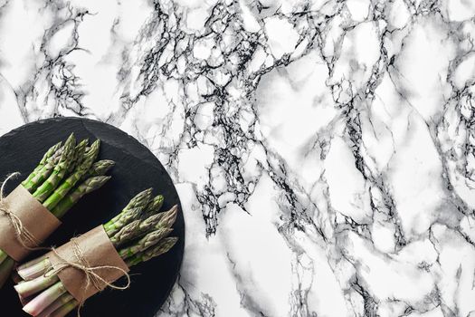 Bunch of an edible, juicy stalks of asparagus on a stone slate, marble background. Fresh, green vegetables, top view. Healthy meal. Spring harvest, agricultural farming concept.