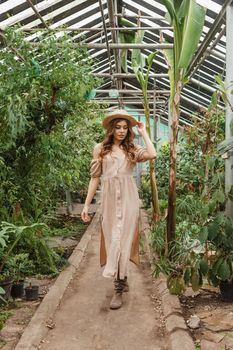 A beautiful young woman takes care of plants in a greenhouse. The concept of gardening and an eco-friendly lifestyle.