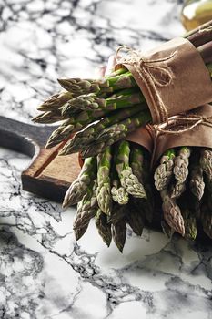 Bunch of an edible, ripe spears of asparagus on a wooden board, marble background. Fresh, green vegetables, top view. Healthy eating. Spring harvest, agricultural farming concept.