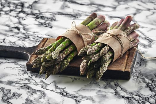 Bunch of an edible, raw stalks of asparagus on a wooden board, marble background. Fresh, green vegetables, top view. Healthy meal. Spring harvest, agricultural farming concept.