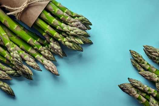 Bunch of an edible, green spears of asparagus isolated on blue background. Fresh vegetables, top view. Healthy eating. Spring harvest, agricultural farming concept.