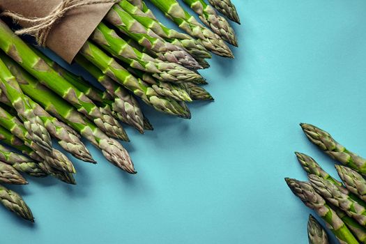 Bunch of an edible, green stalks of asparagus isolated on blue background. Fresh vegetables, top view. Healthy meal. Spring harvest, agricultural farming concept.