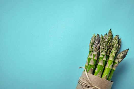Bunch of an edible, ripe spears of asparagus isolated on blue background. Fresh, green vegetables, top view. Healthy eating. Spring harvest, agricultural farming concept.