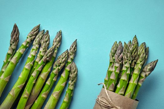 Bunch of an edible, ripe stalks of asparagus isolated on blue background. Fresh, green vegetables, top view. Healthy meal. Spring harvest, agricultural farming concept.