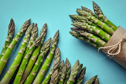 Bunch of an edible, raw sprigs of asparagus isolated on blue background. Fresh, green vegetables, top view. Healthy eating. Spring harvest, agricultural farming concept.
