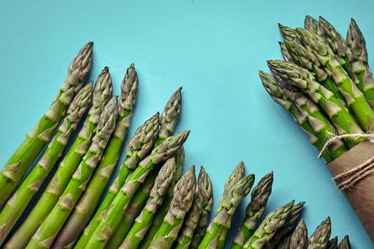 Bunch of an edible, raw stalks of asparagus isolated on blue background. Fresh, green vegetables, top view. Healthy meal. Spring harvest, agricultural farming concept.