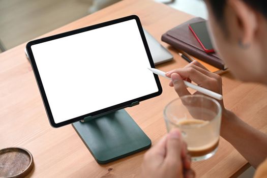 Cropped shot young man drinking coffee and using digital tablet on wooden table.
