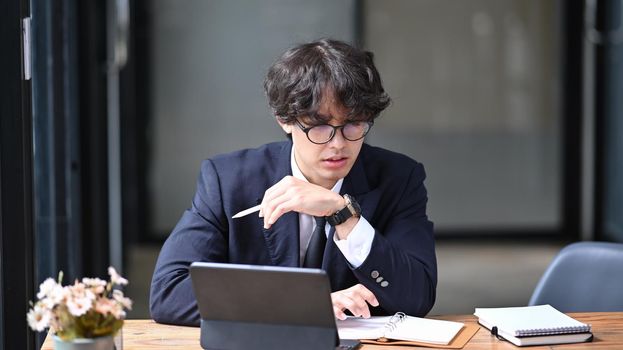 Young asian man in black suit working with computer tablet in office.