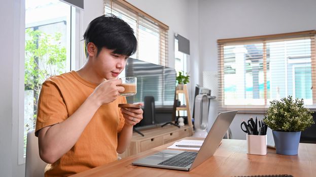 Casual man drinking coffee and using laptop computer at home.