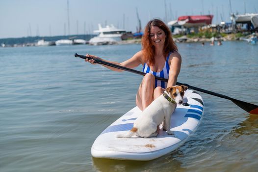 Young red-haired woman on a paddle board with her dog. Surfing.