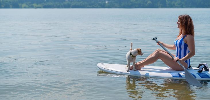 A woman is riding a sup surfboard with a dog on the lake.