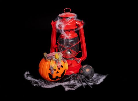 Composition, halloween banner. on a black background, a red kerosene lamp and an orange pumpkin with a funny face with a cobweb. Isolated object, cut object, copy and paste