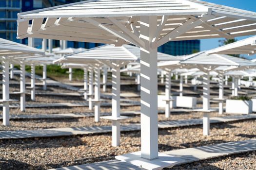 Rows of wooden umbrellas from the sun on the seashore in the morning. Wooden paths on the sand between umbrellas. Beach holiday at the resort