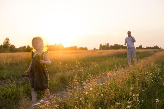 Dad and his blonde daughter are walking and having fun in a chamomile field. The concept of Father's Day, family and nature walks.