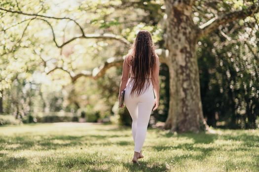 back view of a beautiful woman in a white tracksuit walking in the park with a laptop.