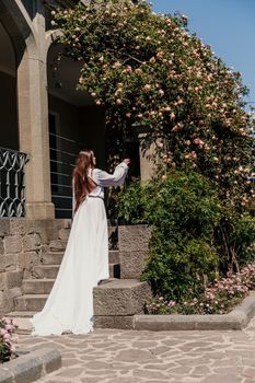 a beautiful woman in a white flowing long dress stay near a beautiful field with pink flowers