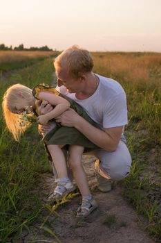 Dad and his blonde daughter are walking and having fun in a chamomile field. The concept of Father's Day, family and nature walks.