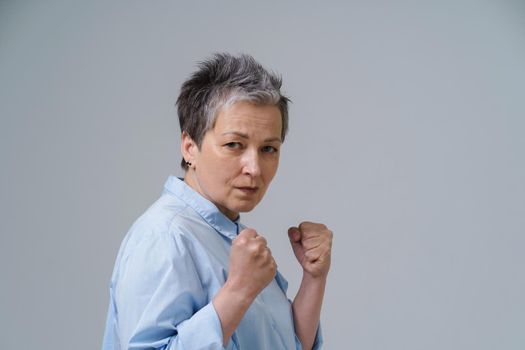 Frightened woman with hands put in fists. Senior woman with grey hair pose as boxing fighter about to stand or protect herself. Human trafficking concept. Confident, strong and aggressive woman.