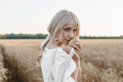 A blonde woman in a long white dress walks in a wheat field. The concept of a wedding and walking in nature.