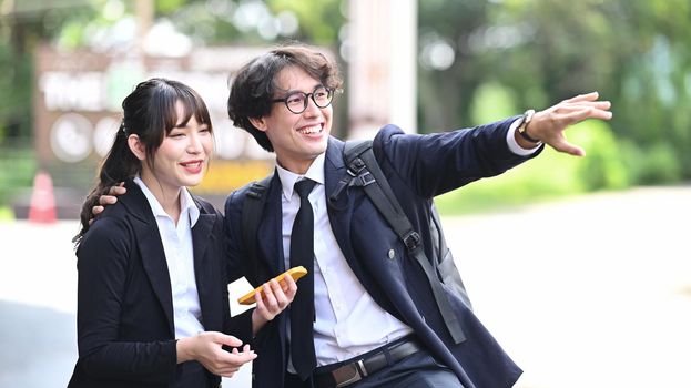 Two cheerful young business people talking to each other while standing outdoors at the city streets.