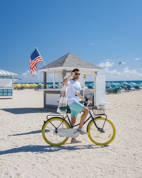 Young men in a swim short on the beach Miami with a bicycle, colorful Miami beach, and a Lifeguard hut in South Beach, Florida.