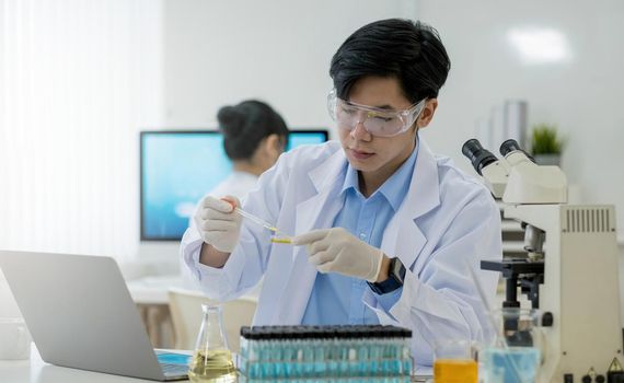 Medical Research Laboratory Portrait of a Handsome Male Scientist Using Digital Tablet Computer, Analysing Liquid Biochemicals in a Laboratory Flask.