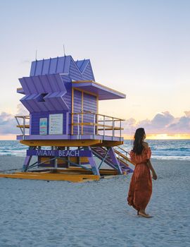 Miami Beach, a couple on the beach at Miami Florida, lifeguard hut Miami Asian women and caucasian men on the beach during sunset. Woman watching sunset on the beach