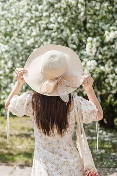 An attractive long-haired woman walks in the spring in the park of blooming apple trees. Spring portrait of a woman