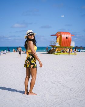 Miami Beach, a couple on the beach at Miami Florida, lifeguard hut Miami Asian women and caucasian men on the beach during sunset. Happy women walking on the white beach