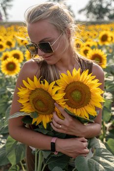 Beautiful woman in sunflower field at sunset enjoying summer nature. Attractive blonde with long healthy hair