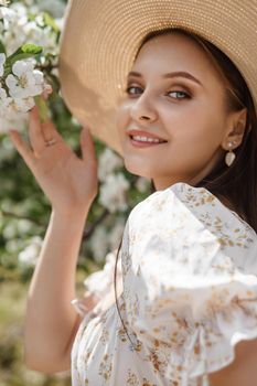 An attractive long-haired woman walks in the spring in the park of blooming apple trees. Spring portrait of a woman