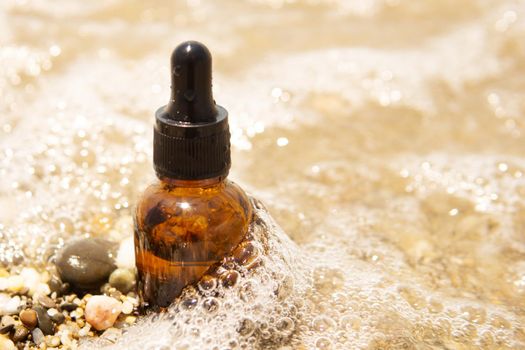 Cosmetic serum for the skin in a glass bottle. A bottle with an eyedropper on a pebble beach by the sea. Essences for skin care on the background of stones. The concept of natural cosmetics and SPA products.