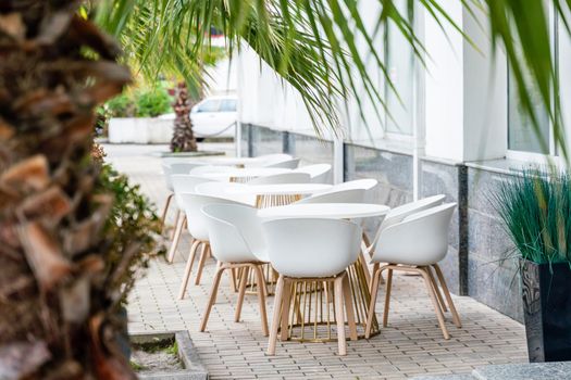 Street cafe with white chairs, green foliage around. Without people, tourism, travel