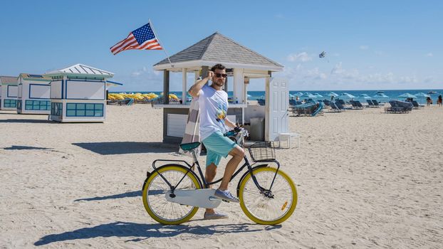 Young men in a swim short on the beach Miami with a bicycle, colorful Miami beach, and a Lifeguard hut in South Beach, Florida.