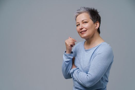 Mature woman 50s with grey hair posing with hands folded and copy space on left isolated on white background. Copy space and place for product placement. Mature people healthcare concept.