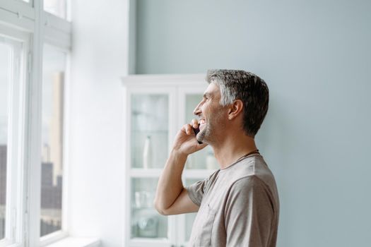 smiling man talking on a smartphone standing near the window . close-up.