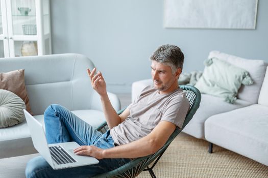 mature man using a laptop while sitting in a home chair. side view.