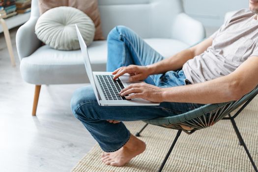 cropped image of a man using a laptop while sitting in a chair. side view.