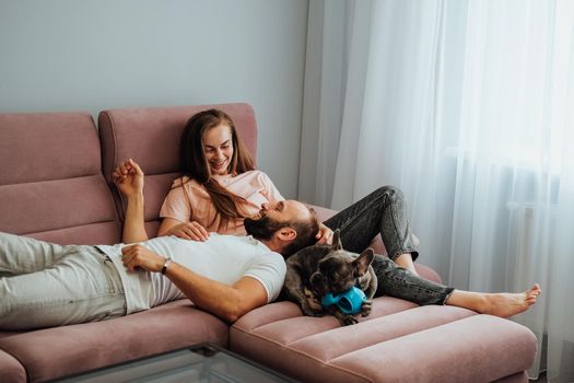Adult Couple Having Leisure with French Bulldog at Home, Cheerful Woman and Man Relaxing on Pink Sofa with Their Pet