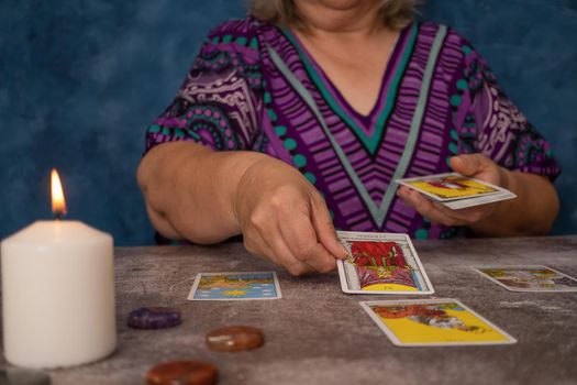 older white-haired woman reading tarot cards on a wooden table with candle