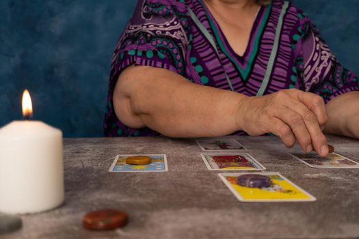 older white-haired woman reading tarot cards on a wooden table with candle