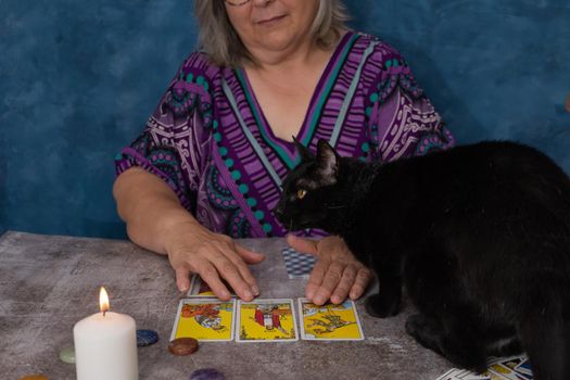 older white-haired woman reading tarot cards on a wooden table with candle