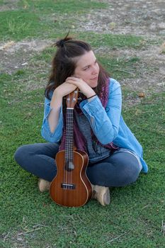 young brunette girl with long hair playing ukulele in the field on the grass