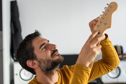 young boy with beard playing guitar at home with piano on the back